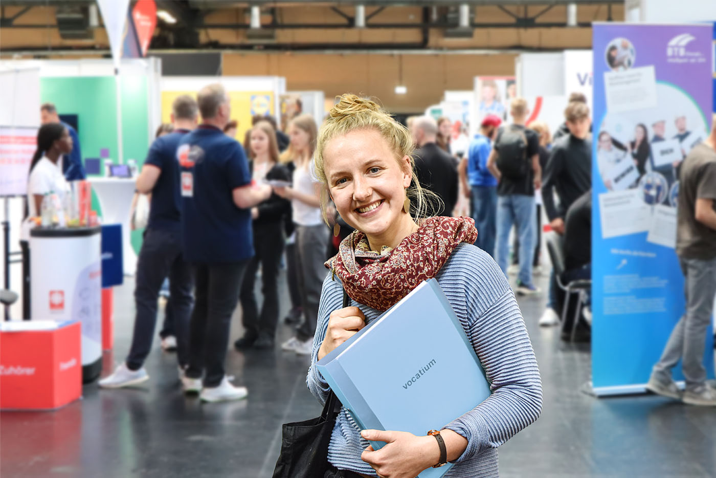 Frau schaut in die Kamera, lacht und hält eine blaue Mappe in der Hand