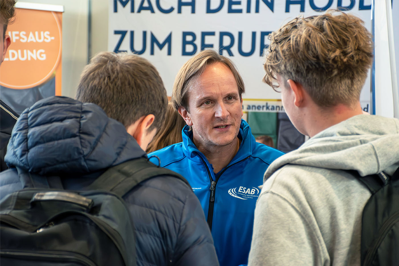 Mann in blauer Jacke unterhält sich mit zwei jungen Männern