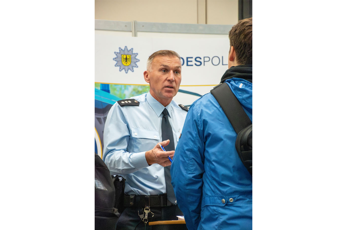 Polizist in Uniform unterhält sich am Messestand mit jungem Mann