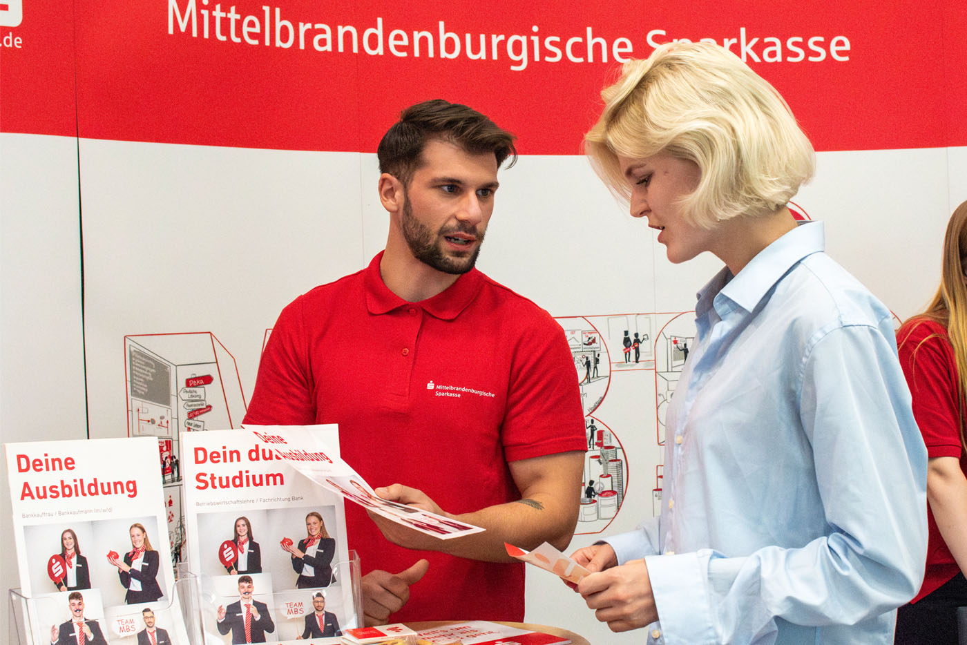 Mann in rotem T-Shirt unterhält sich am Messestand mit Frau